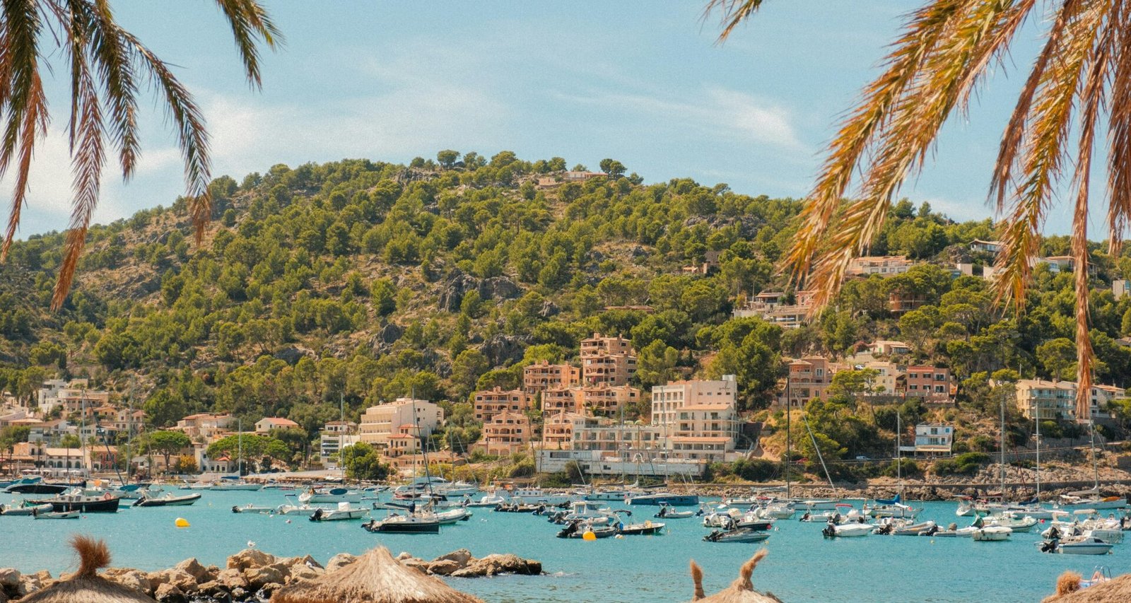 Boote in einer Bucht auf Mallorca mit Palmen, Gebäuden und klarem Wasser, aufgenommen von Alexis Presa.
