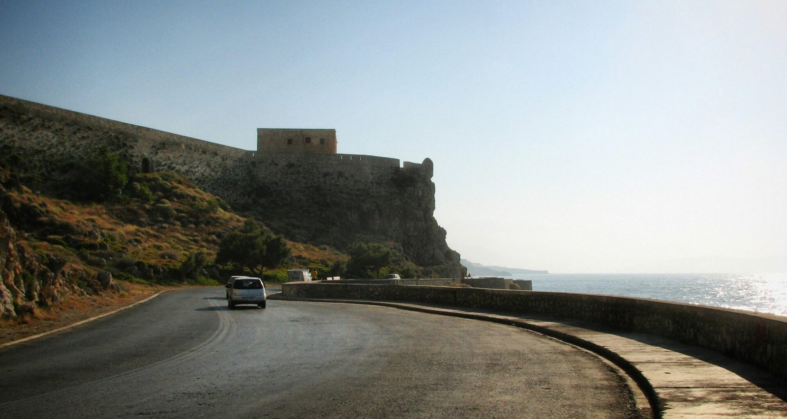 Ein Auto fährt auf Mallorca auf einer Küstenstraße in Richtung einer historischen Festung, aufgenommen von Sergei Gussev.