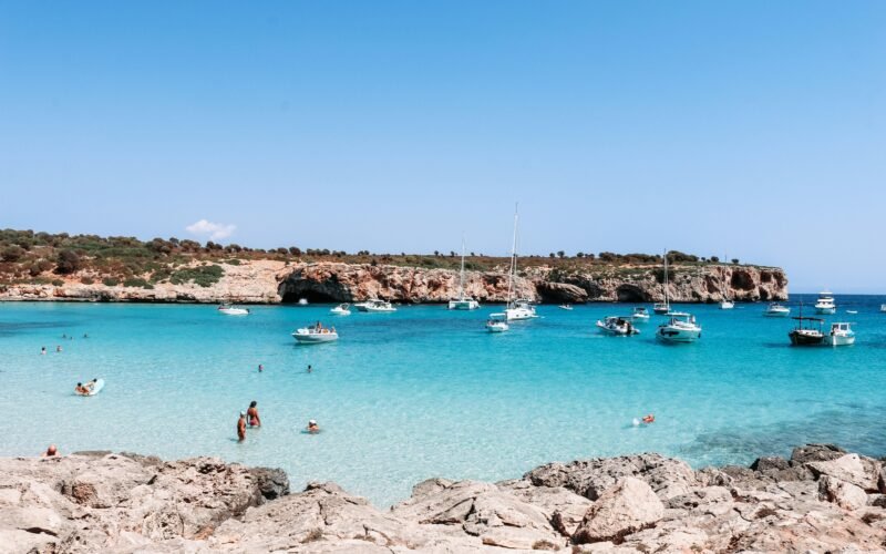 Menschen schwimmen tagsüber im klaren Wasser auf Mallorca am Strand, aufgenommen von Austin Farrington.
