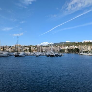 Yachten liegen im Hafen auf Mallorca vor der Stadt mit Hochhäusern und Segelbooten, aufgenommen von David Vives.