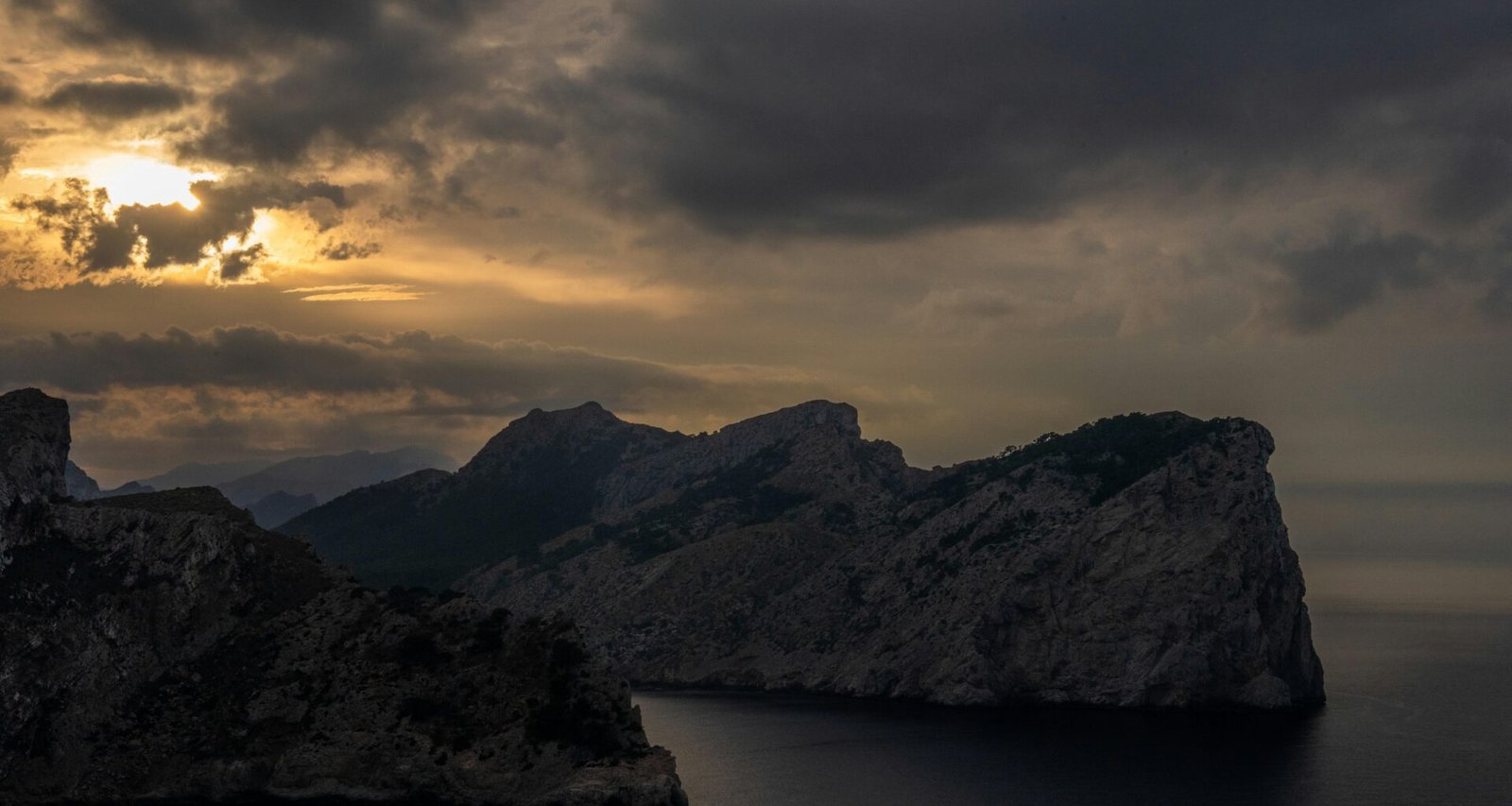 Felsige Küste auf Mallorca unter dunklem, stürmischem Sonnenuntergangshimmel, fotografiert von Tim Bernhard
