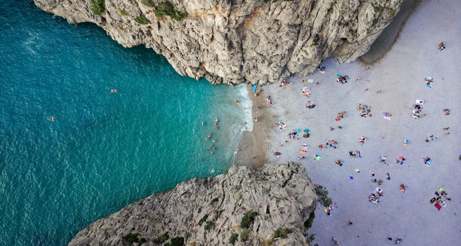 Menschen schwimmen im klaren Wasser eines Strandes auf Mallorca, während die Sonne scheint, aufgenommen von Alex Kulikov.