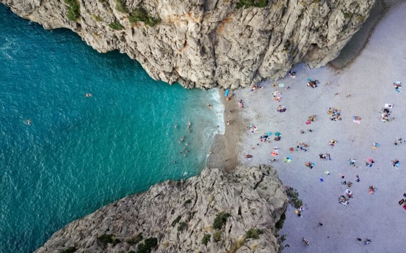 Menschen schwimmen im klaren Wasser eines Strandes auf Mallorca, während die Sonne scheint, aufgenommen von Alex Kulikov.