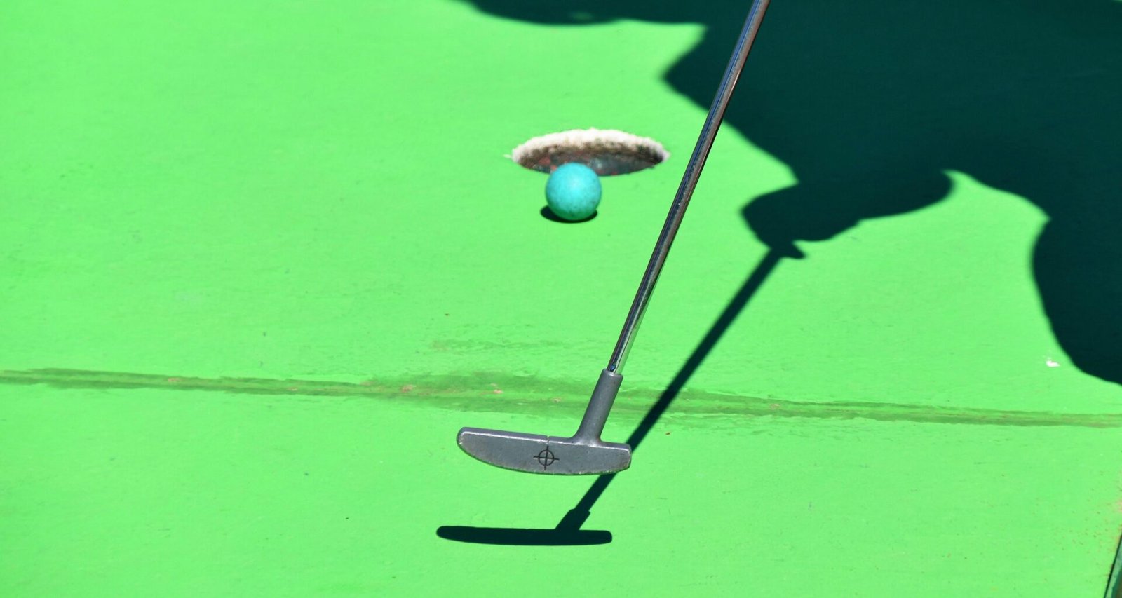 Person beim Golfabschlag auf Mallorca, Ball kurz vor dem Loch, im Hintergrund grüner Rasen