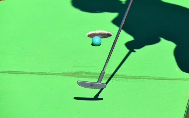 Person beim Golfabschlag auf Mallorca, Ball kurz vor dem Loch, im Hintergrund grüner Rasen