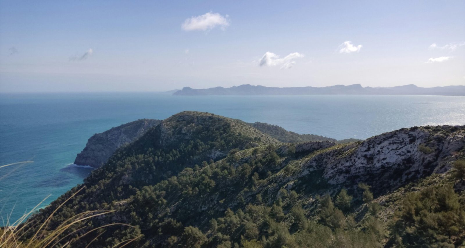 Blick auf das Meer auf Mallorca von einem Hügel aus, mit weiten Wasserflächen und Himmel im Hintergrund