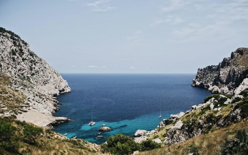 Boot liegt vor einer Insel auf Mallorca, fotografiert von Oscar Nord, mit klarem Wasser und ruhiger Umgebung
