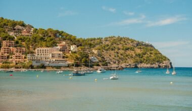 Boote liegen in einer Bucht auf Mallorca, im Hintergrund eine Küstenstadt auf einem Hügel sichtbar