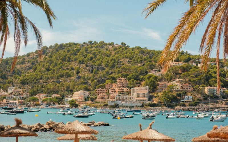 Boote liegen in einer Bucht auf Mallorca, umgeben von Palmen und Gebäuden, aufgenommen von Alexis Presa.