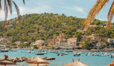 Boote in einer Bucht auf Mallorca, umgeben von Palmen und Gebäuden, aufgenommen von Alexis Presa.