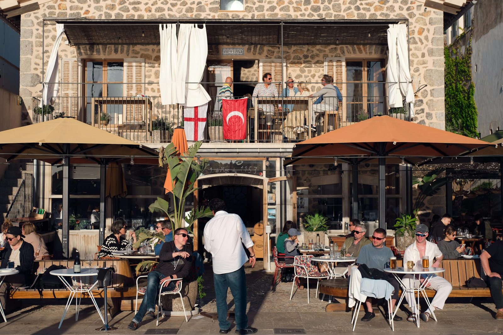 Menschen sitzen an einem Außenbereich eines Cafés auf Mallorca und genießen das Essen und die Gesellschaft.