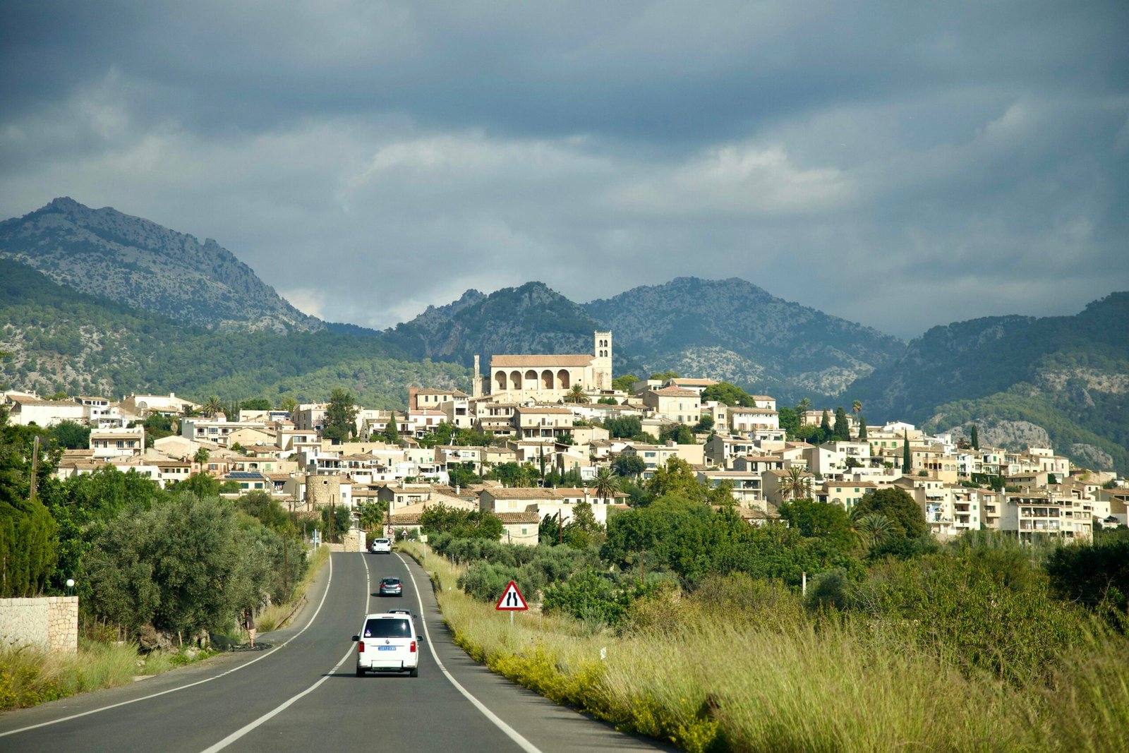 Ein Auto fährt auf Mallorca auf einer Straße mit Stadt im Hintergrund, aufgenommen von Stock Birken.