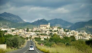 Ein Auto fährt auf Mallorca eine Straße entlang mit einer Stadt im Hintergrund, aufgenommen von Stock Birken