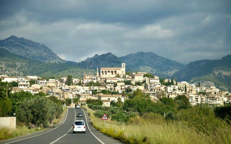 Ein Auto fährt auf Mallorca eine Straße entlang mit einer Stadt im Hintergrund, aufgenommen von Stock Birken