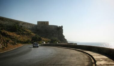 Ein Auto fährt auf Mallorca auf einer Küstenstraße in Richtung einer historischen Festung, aufgenommen von Sergei Gussev.