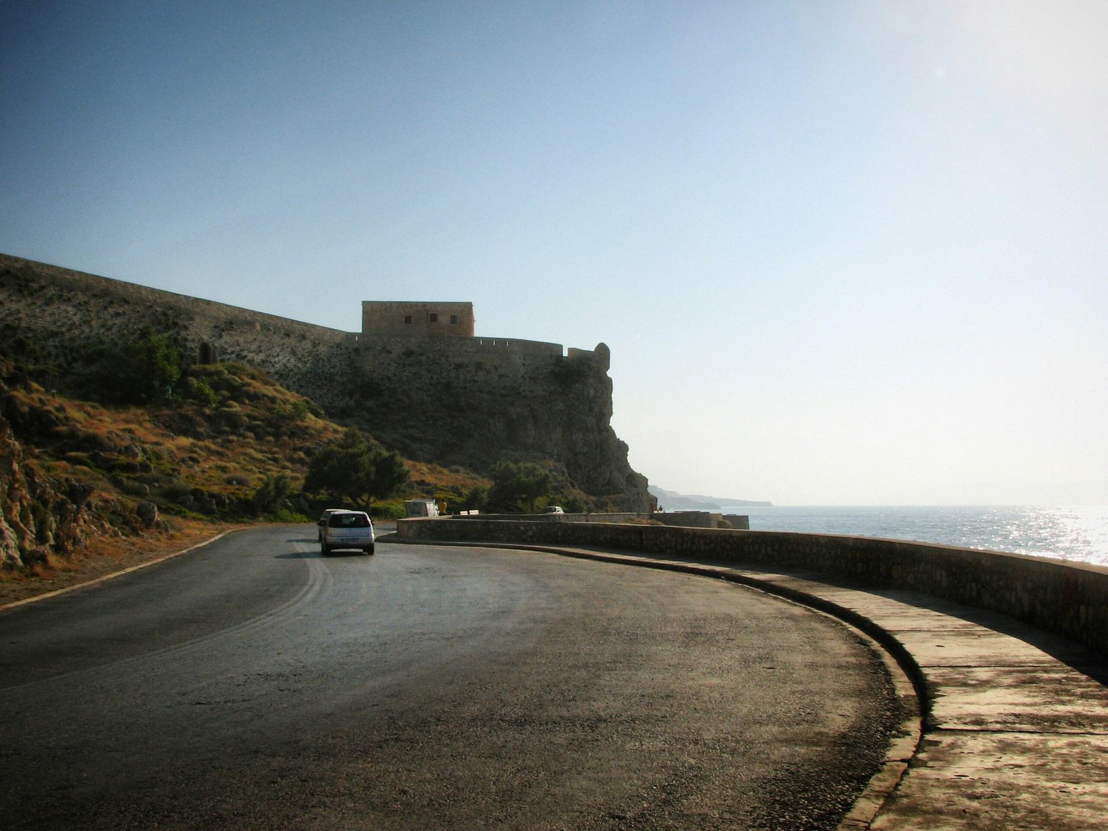 Ein Auto fährt auf Mallorca auf einer Küstenstraße in Richtung einer historischen Festung, aufgenommen von Sergei Gussev.