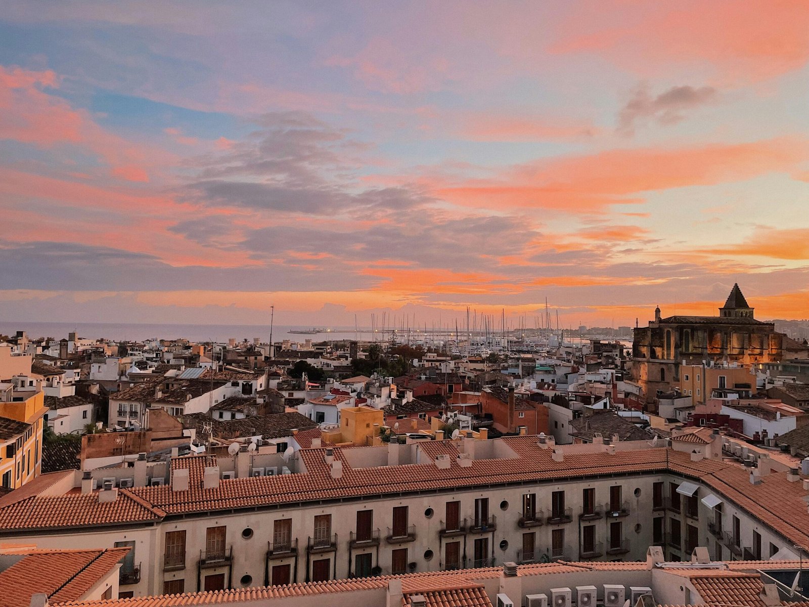 Sonnenuntergang über einer Stadt auf Mallorca, gesehen von einem Dach aus, mit warmen Farben am Himmel