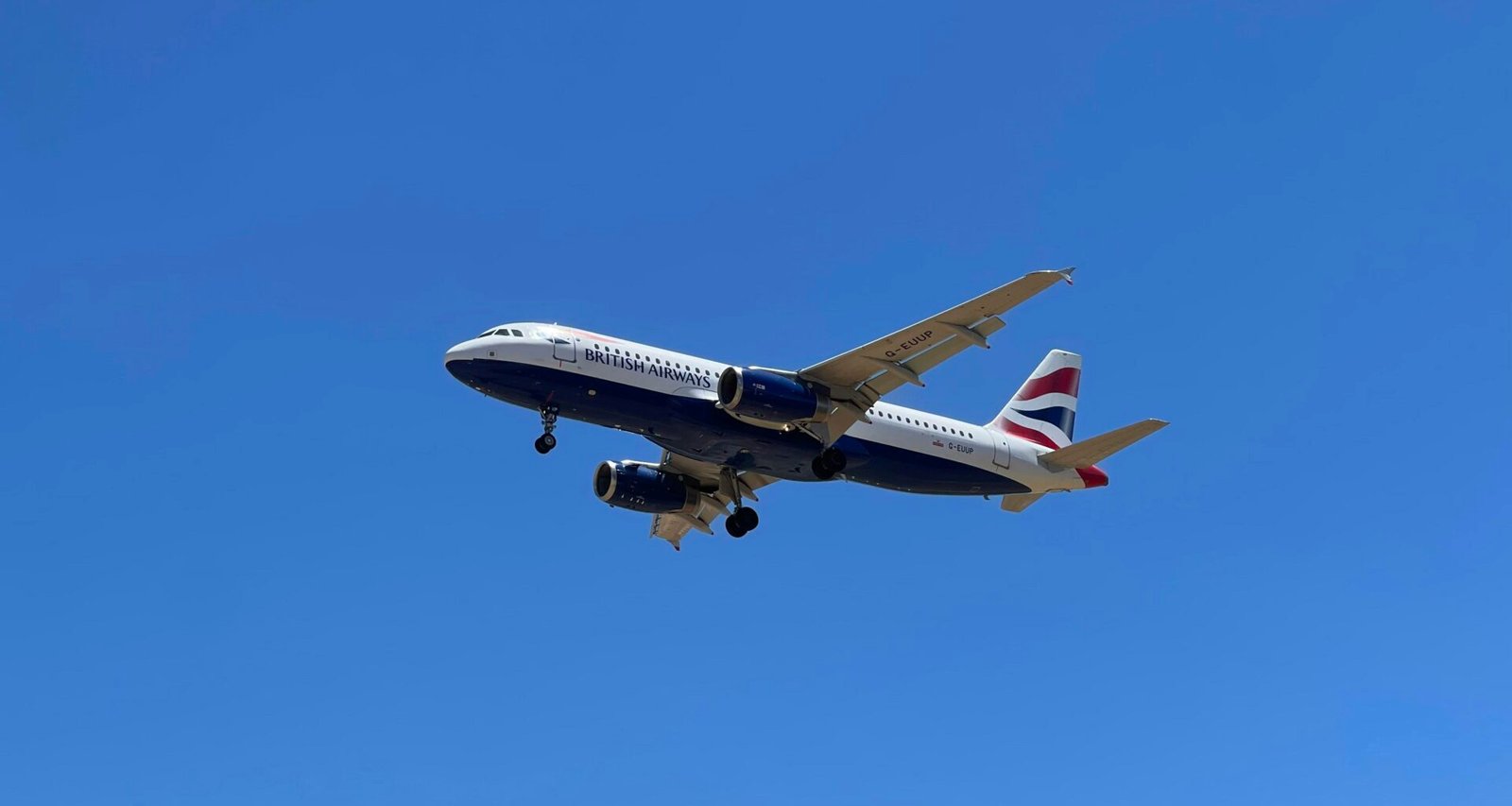 Ein Flugzeug fliegt hoch am Himmel auf Mallorca, fotografiert von John Cameron, mit blauer Himmel im Hintergrund.