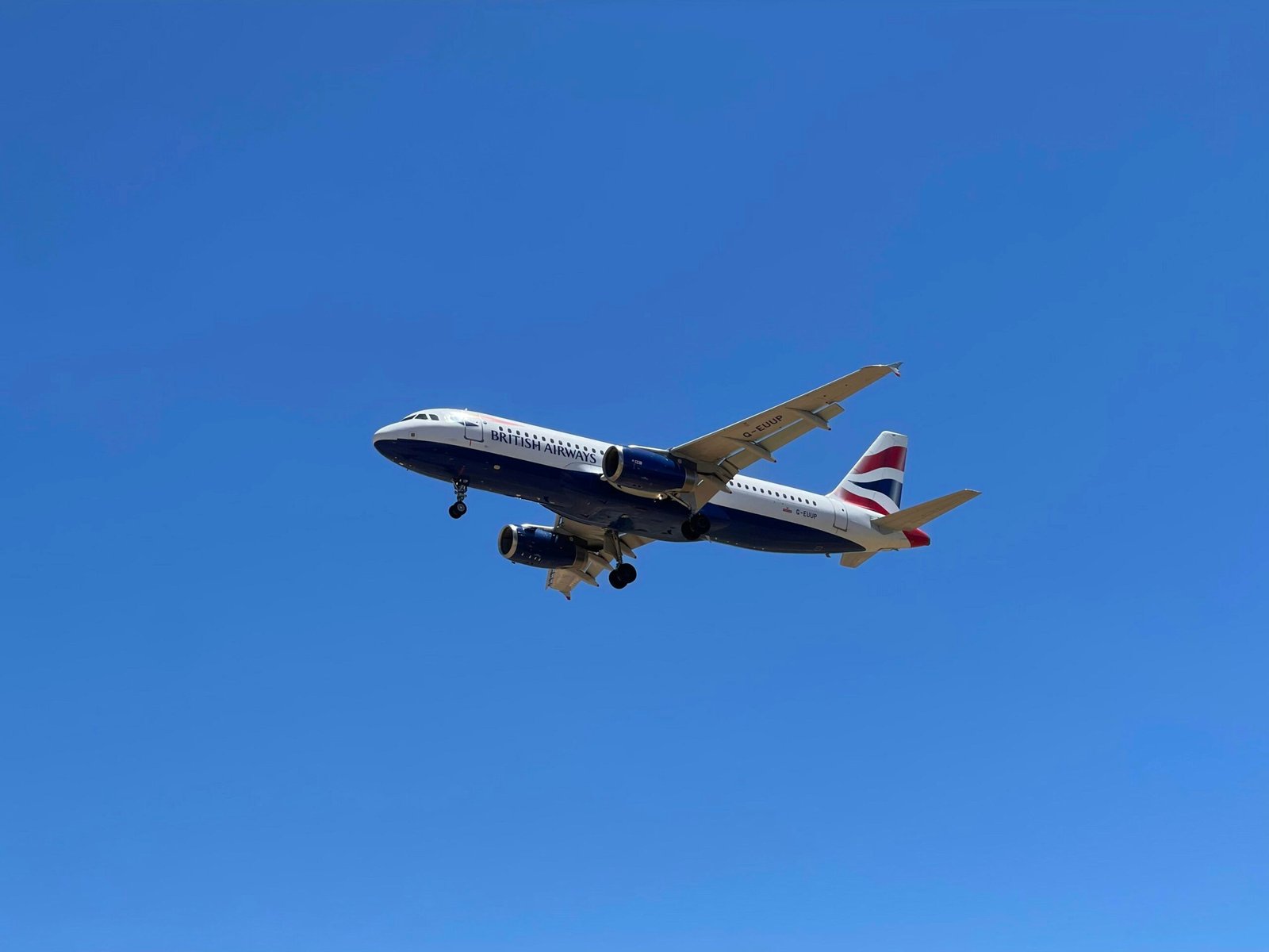 Ein Flugzeug fliegt hoch am Himmel auf Mallorca, fotografiert von John Cameron, mit blauer Himmel im Hintergrund.