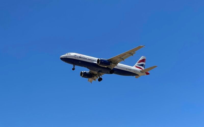 Ein Flugzeug fliegt am Himmel auf Mallorca, aufgenommen von John Cameron, mit Blick auf die Insel im Hintergrund.