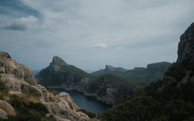 Ein Fluss, der durch ein grünes Tal auf Mallorca fließt, umgeben von Bergen und Vegetation, aufgenommen von Alex Foret.