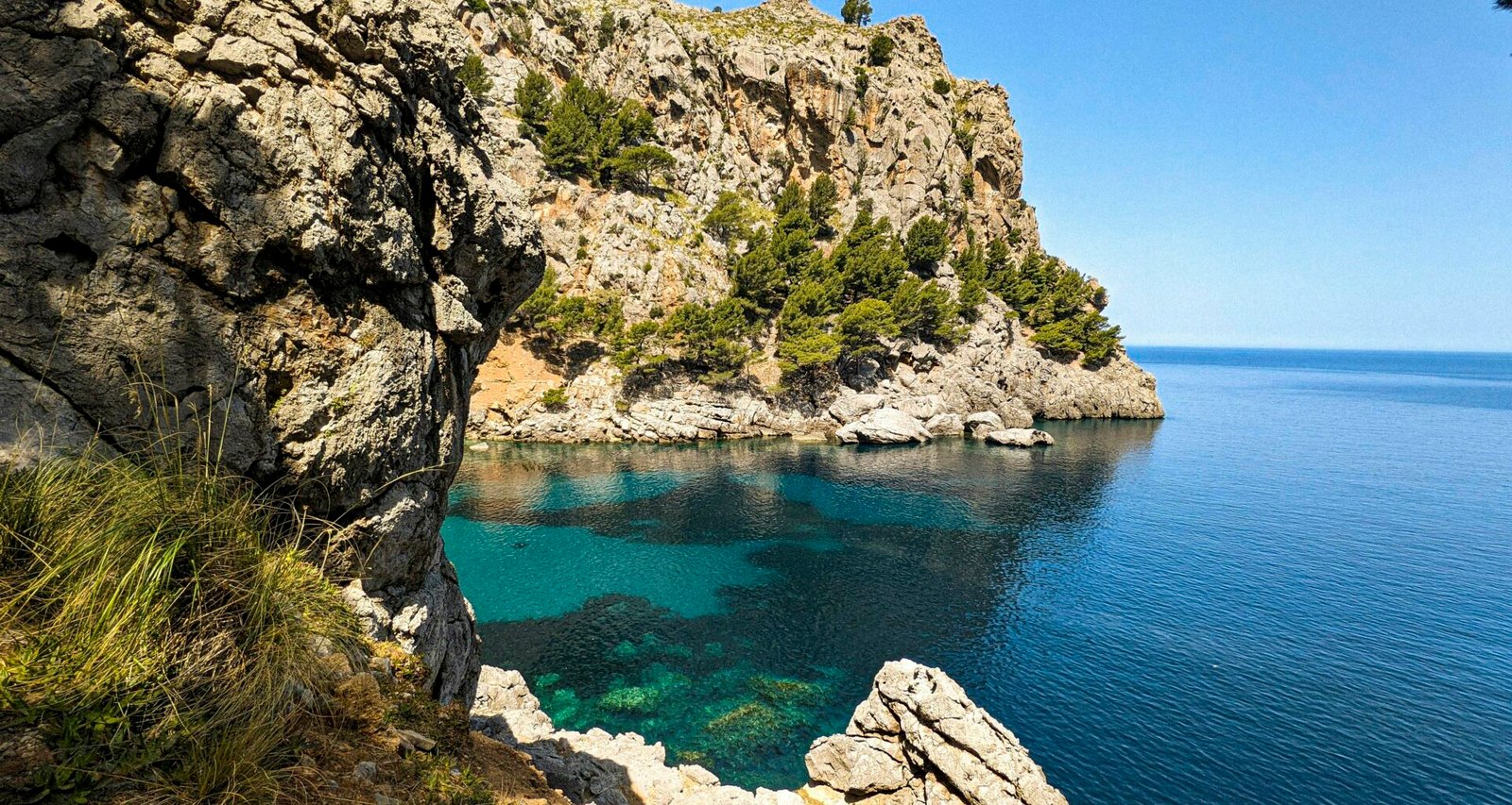 Klares Wasser vor einer felsigen Klippe auf Mallorca, aufgenommen von Andre Blanco, zeigt die natürliche Küstenlandschaft.