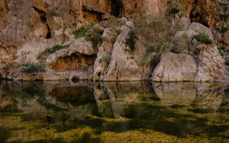 Ein Gewässer auf Mallorca, umgeben von Felsen und Gras, aufgenommen von Mariya, zeigt die ruhige Natur der Insel.