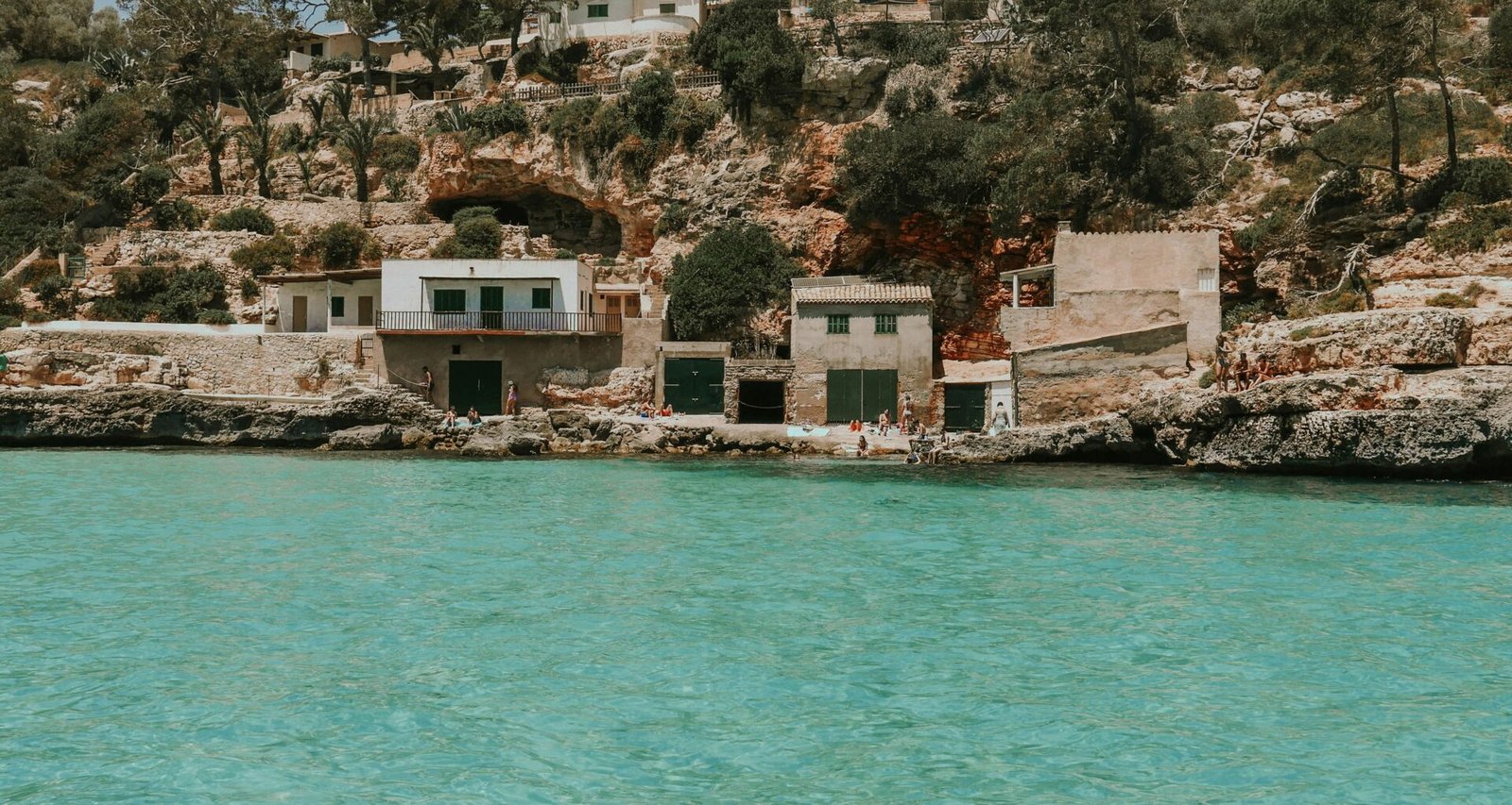 Ein Haus auf einer Klippe auf Mallorca mit Blick auf das Wasser im Hintergrund, fotografiert von Shery Arturova.