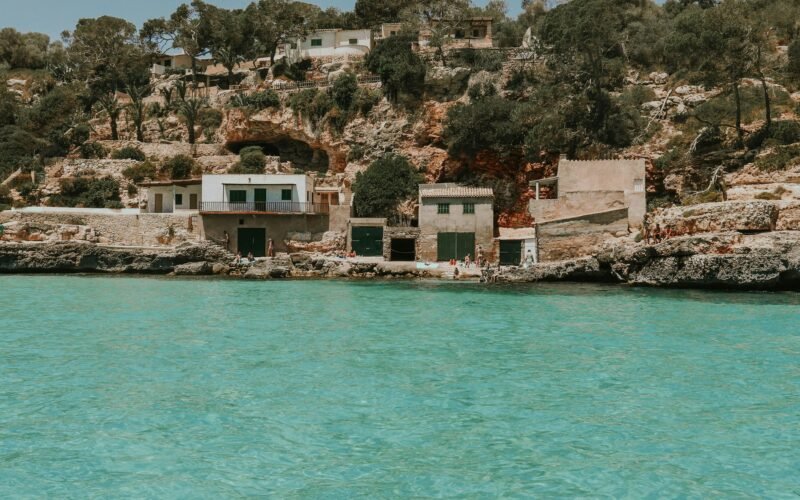 Ein Haus auf einer Klippe auf Mallorca mit Blick auf das Wasser im Hintergrund, fotografiert von Shery Arturova.