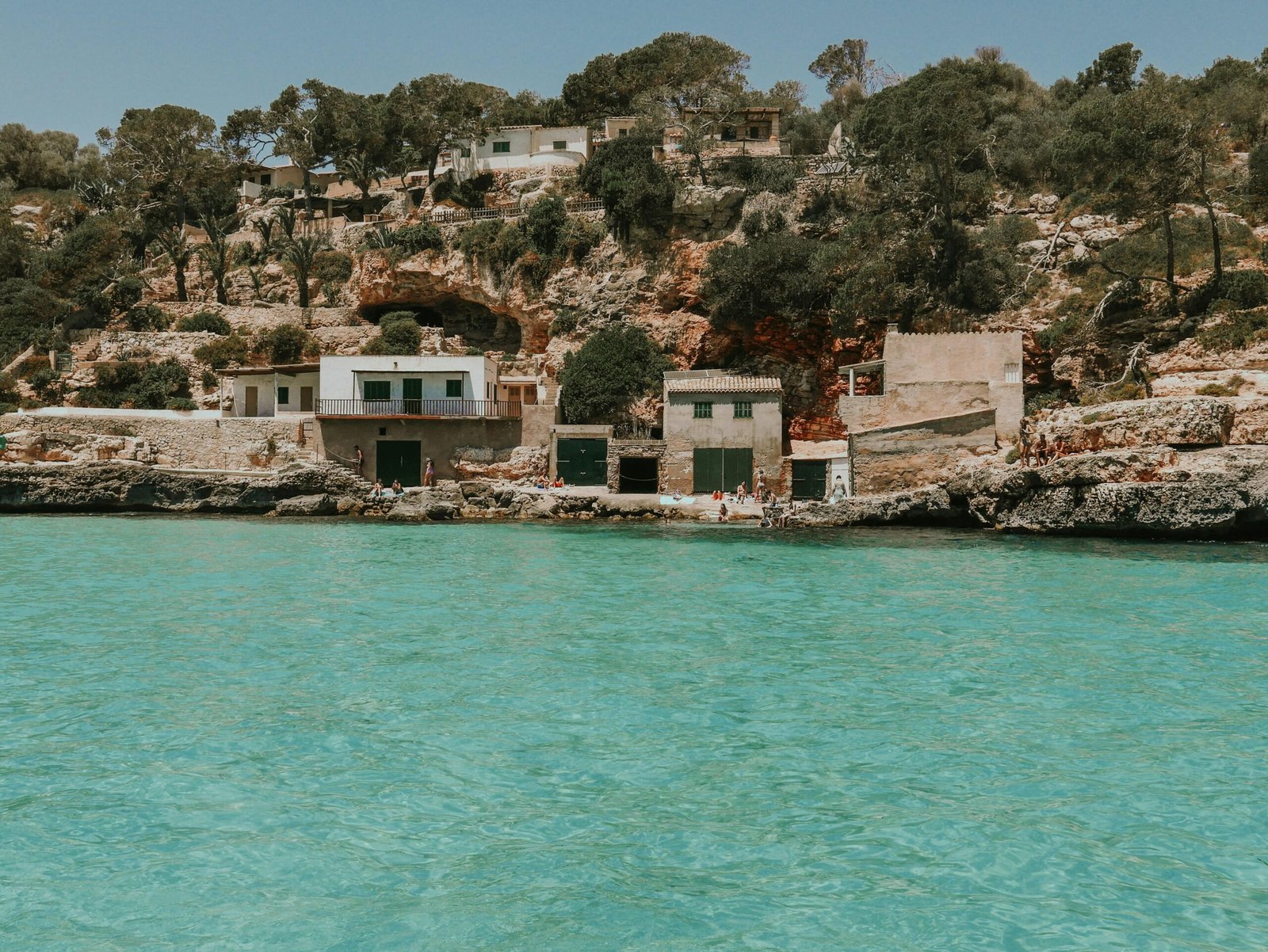 Ein Haus auf einer Klippe auf Mallorca mit Blick auf das Wasser im Hintergrund, fotografiert von Shery Arturova.