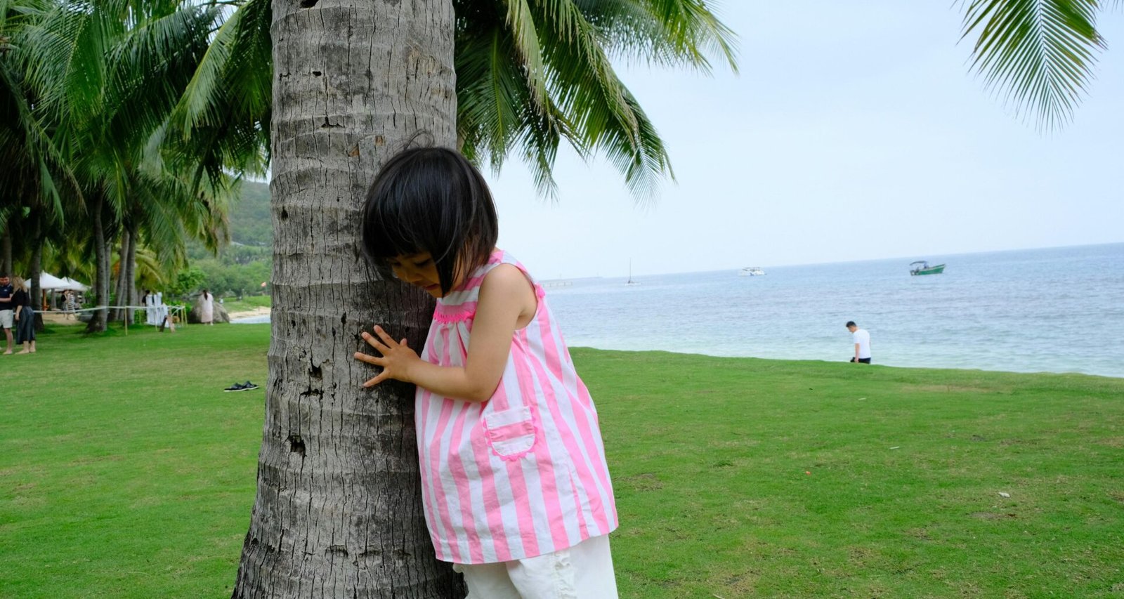 Kleines Mädchen versteckt sich hinter einer Palme auf Mallorca, umgeben von grünen Blättern und natürlicher Umgebung.