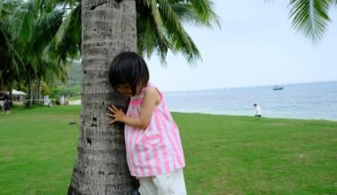 Kleines Mädchen versteckt sich hinter einer Palme auf Mallorca, umgeben von grünen Blättern und natürlicher Umgebung.