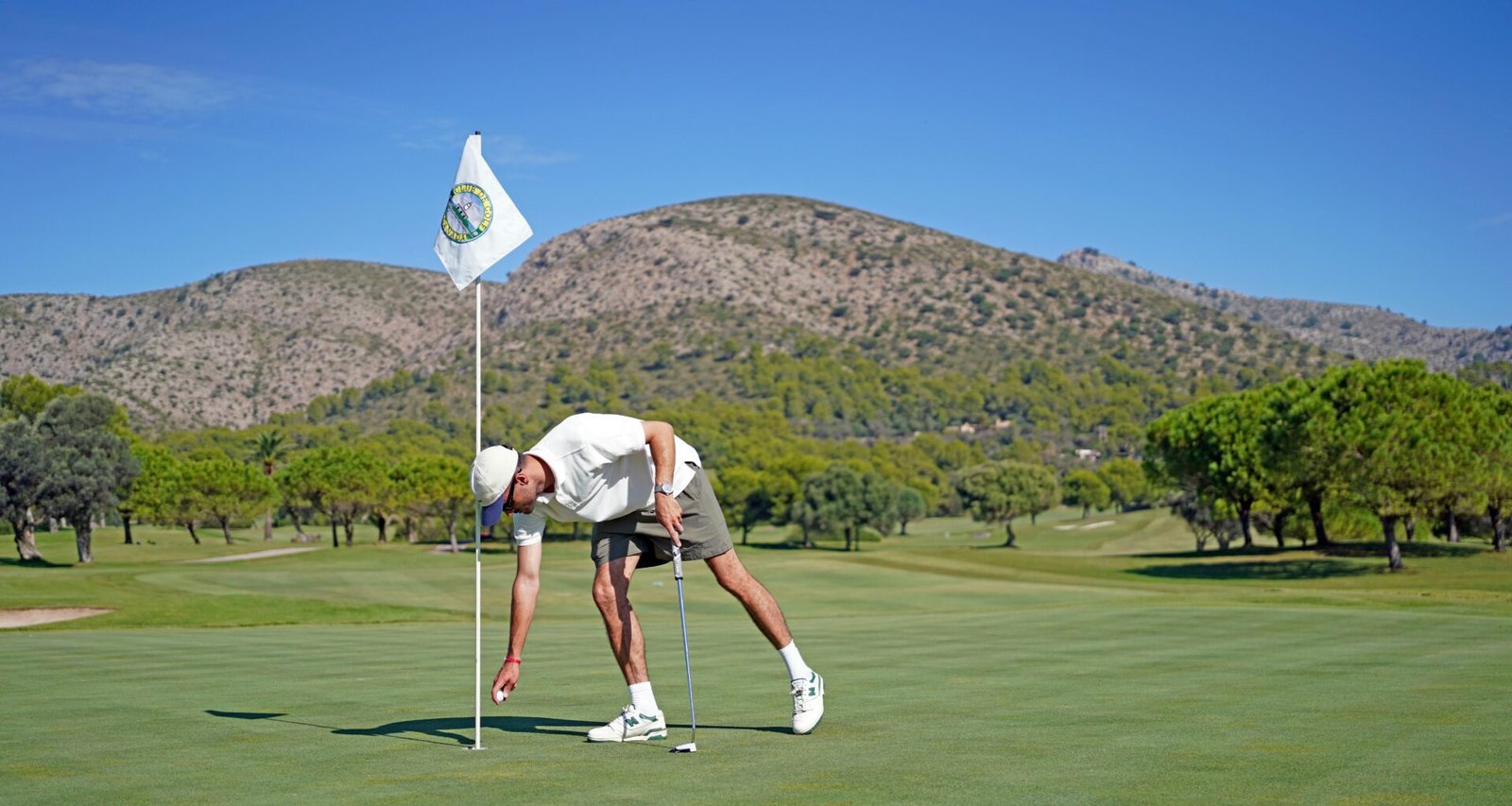 Mann beim Golf auf Mallorca, der den Ball ins Loch legt, aufgenommen von Frederik Rosar