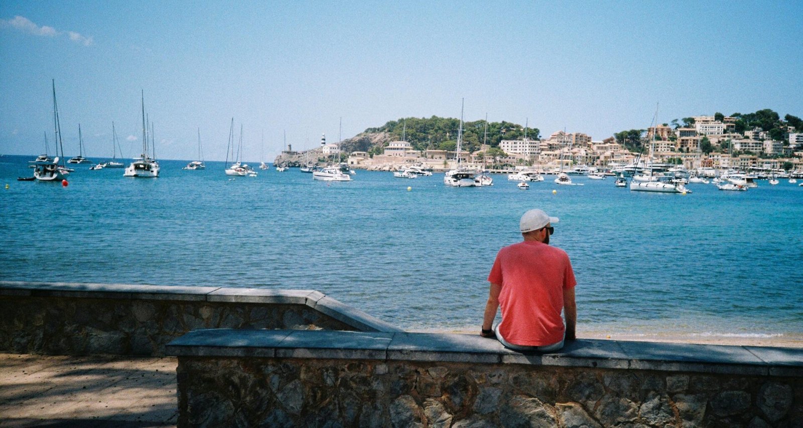 Mann sitzt auf Mallorca auf einer Mauer und blickt auf das Wasser, umgeben von natürlicher Kulisse