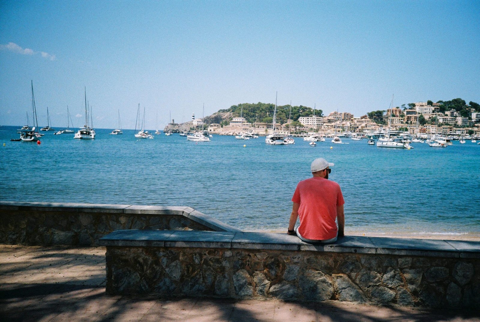 Mann sitzt auf Mallorca auf einer Mauer und blickt auf das Wasser, die Küste im Hintergrund, aufgenommen von Nick Page.