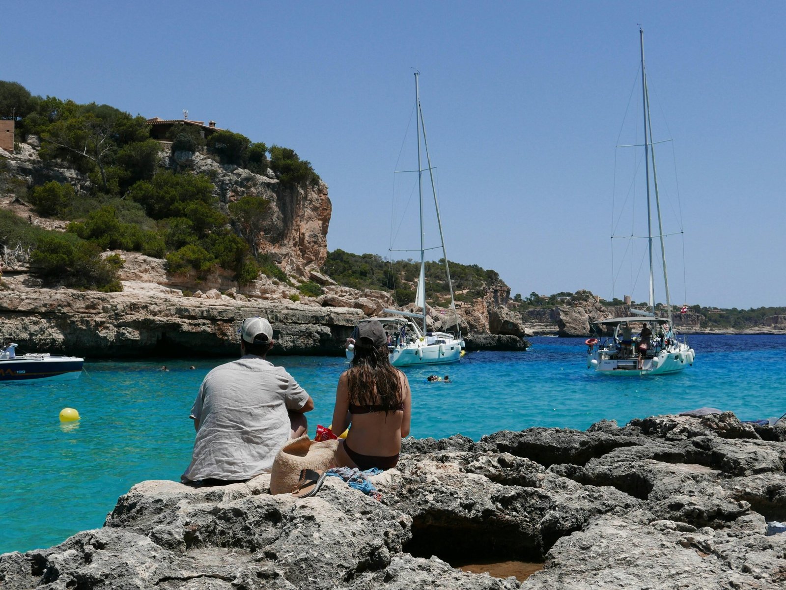 Ein Mann und eine Frau sitzen auf Felsen und schauen auf das Wasser auf Mallorca, aufgenommen von Shery Arturova.