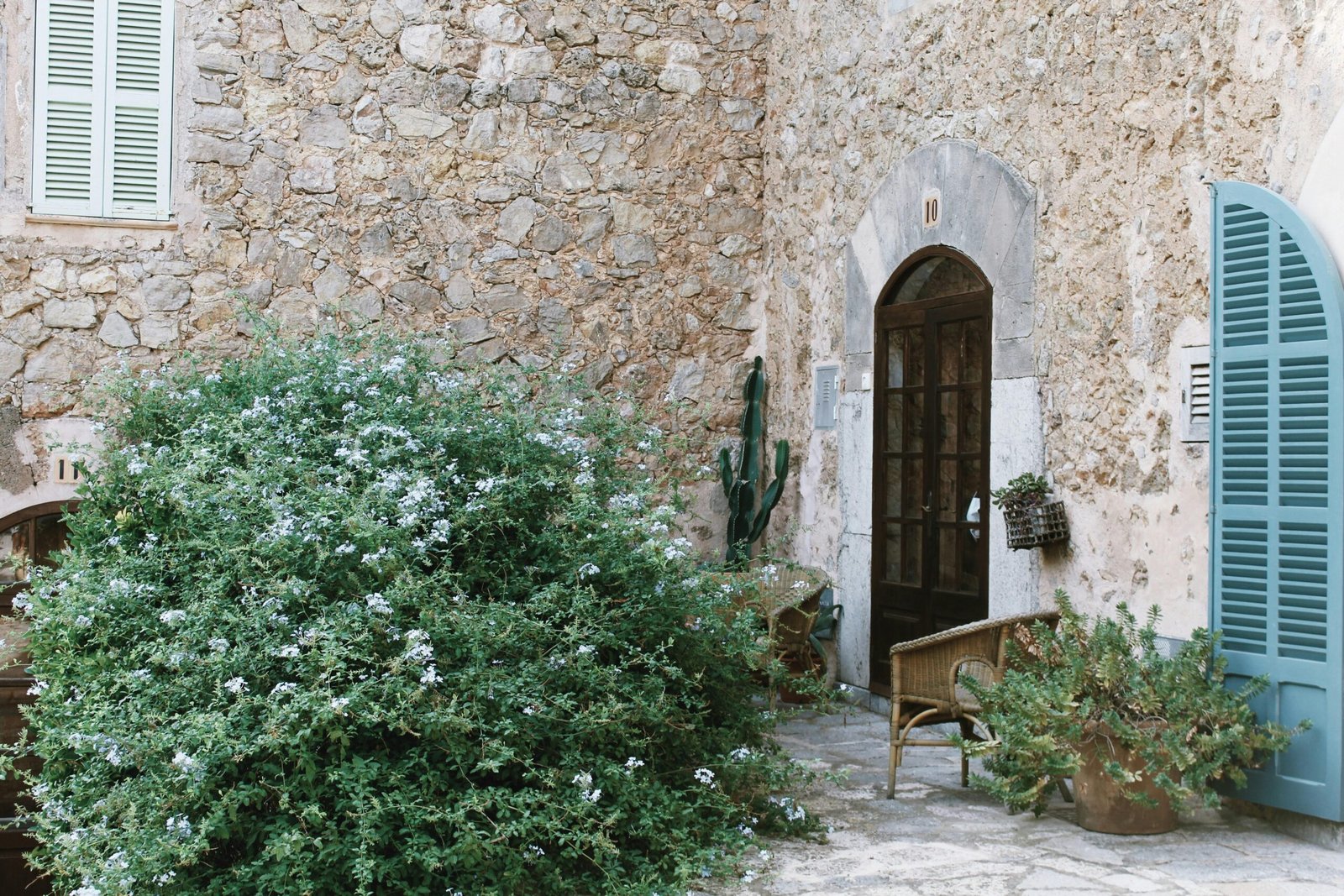 Ein Steinhaus mit blauen Fensterläden neben einem Busch auf Mallorca, aufgenommen von Chloe Frost-Smith