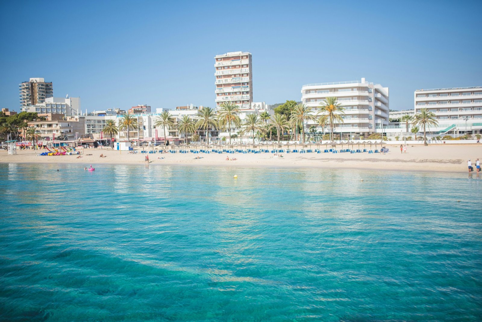 Strand auf Mallorca mit Gebäuden im Hintergrund, aufgenommen von Monika Guzikowska.