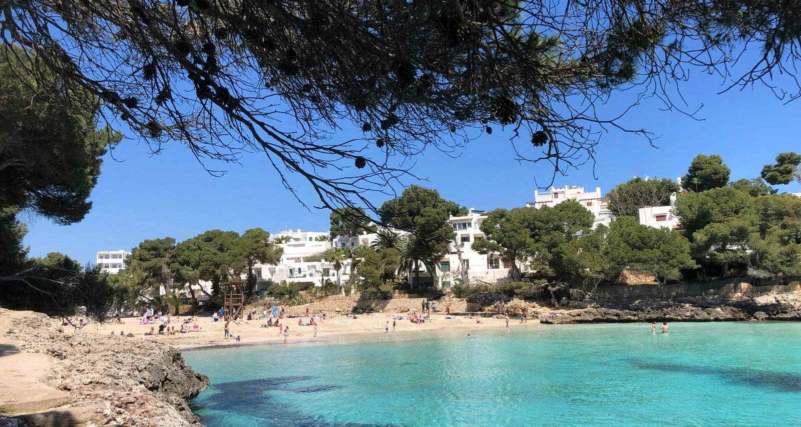Ein Strand auf Mallorca mit Menschen, die am Wasser liegen und die Sonne genießen, fotografiert von yelr.