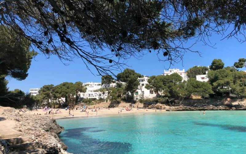 Ein Strand auf Mallorca mit Menschen, die am Wasser liegen und die Sonne genießen, fotografiert von yelr.