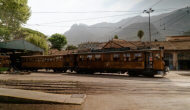 Ein Zug fährt an einem Bahnhof auf Mallorca vorbei, umgeben von Bergen und Natur, fotografiert von Victor Oonk.