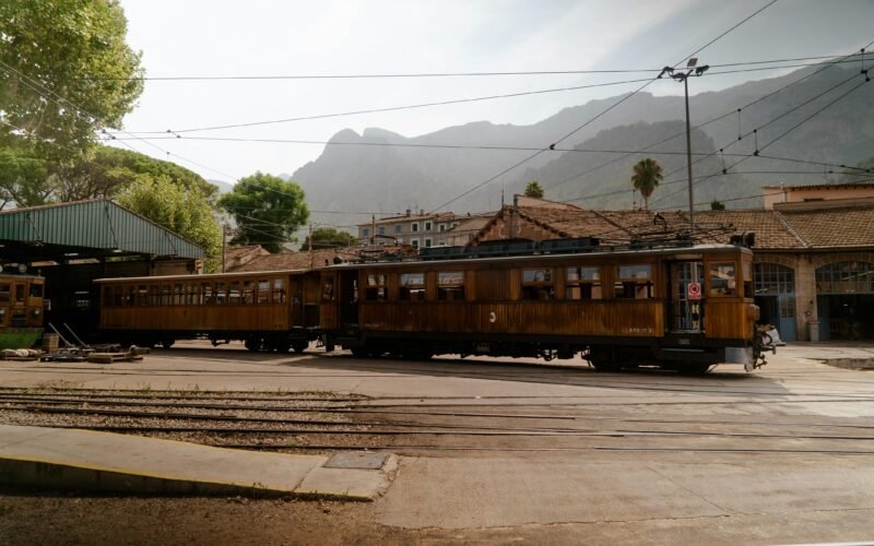 Ein Zug fährt an einem Bahnhof auf Mallorca vorbei, umgeben von Bergen und Natur, fotografiert von Victor Oonk.