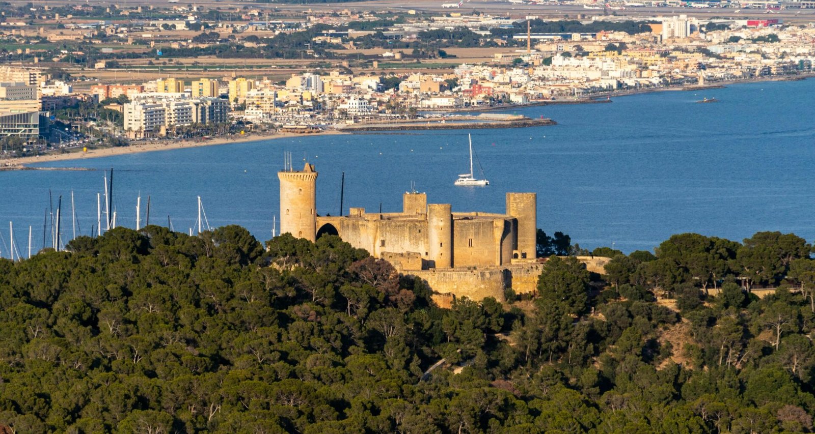 Eine Burg auf einem Hügel auf Mallorca mit Blick auf ein ruhiges Gewässer, aufgenommen von David Vives.
