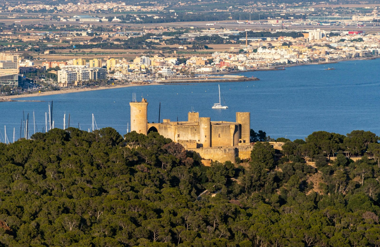 Eine Burg auf einem Hügel auf Mallorca mit Blick auf ein ruhiges Gewässer, aufgenommen von David Vives.