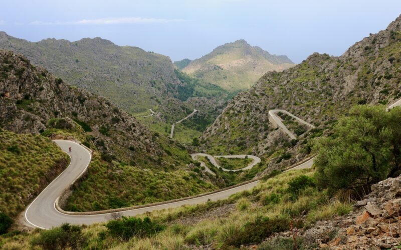 Winding road in den Bergen auf Mallorca, umgeben von üppigem Grün und Natur, fotografiert von Alexandra Zelena.