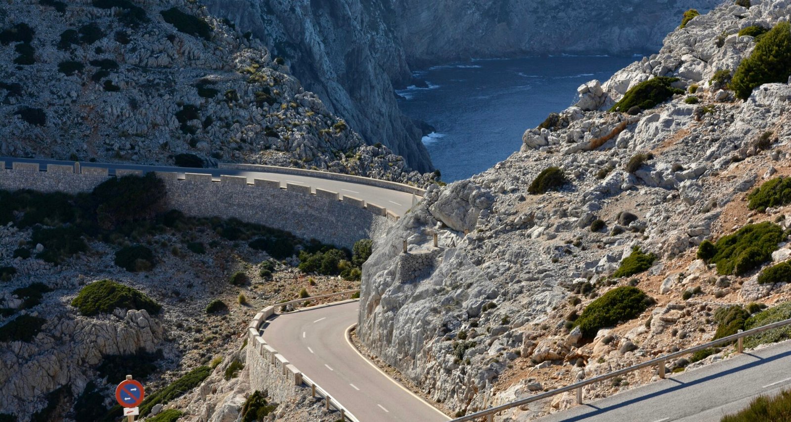 Eine gewundene Straße an den Berghängen auf Mallorca, umgeben von Natur und felsigen Landschaften.