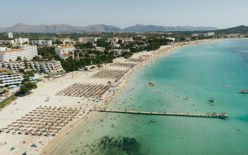 Pitoreske Strandansicht auf Mallorca mit Touristen und Gebäuden, fotografiert von Tomas Eidsvold.