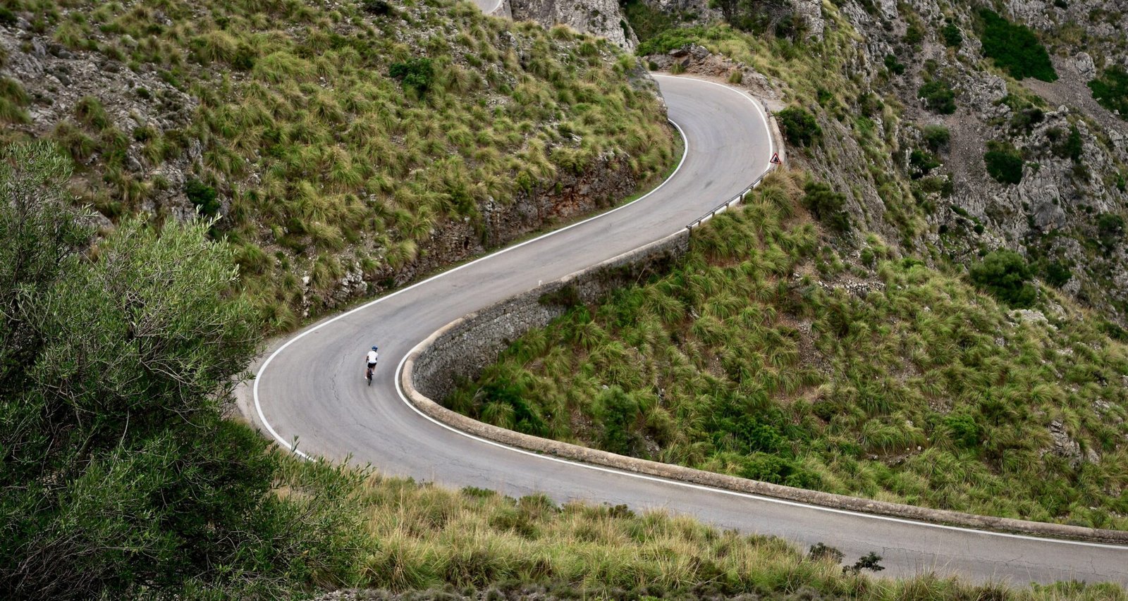 Person fährt auf Mallorca mit dem Motorrad eine kurvige Straße entlang, umgeben von Natur und Landschaft.