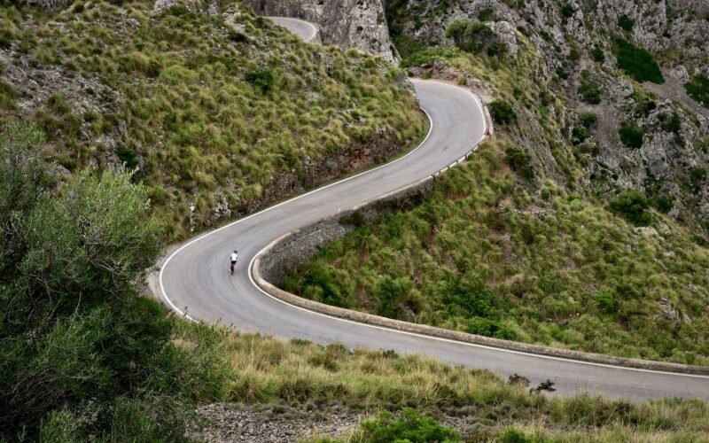 Person fährt auf Mallorca mit dem Motorrad eine kurvige Straße entlang, umgeben von Natur und Landschaft.
