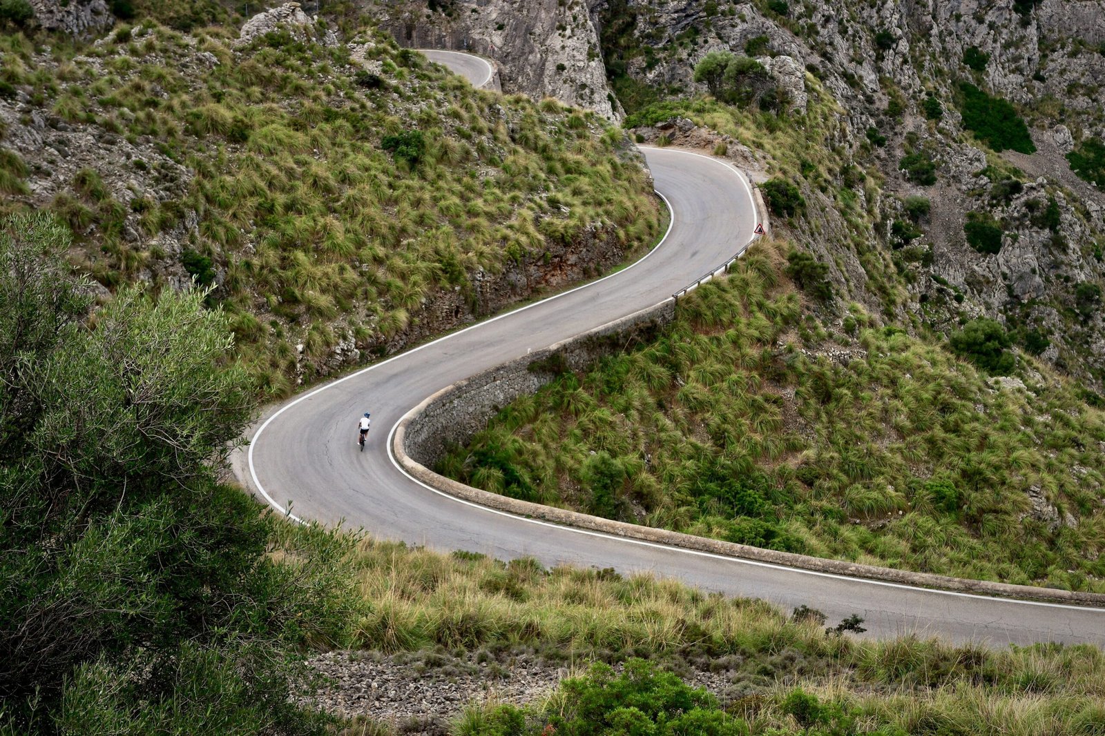 Person fährt auf Mallorca mit dem Motorrad eine kurvige Straße entlang, umgeben von Natur und Landschaft.